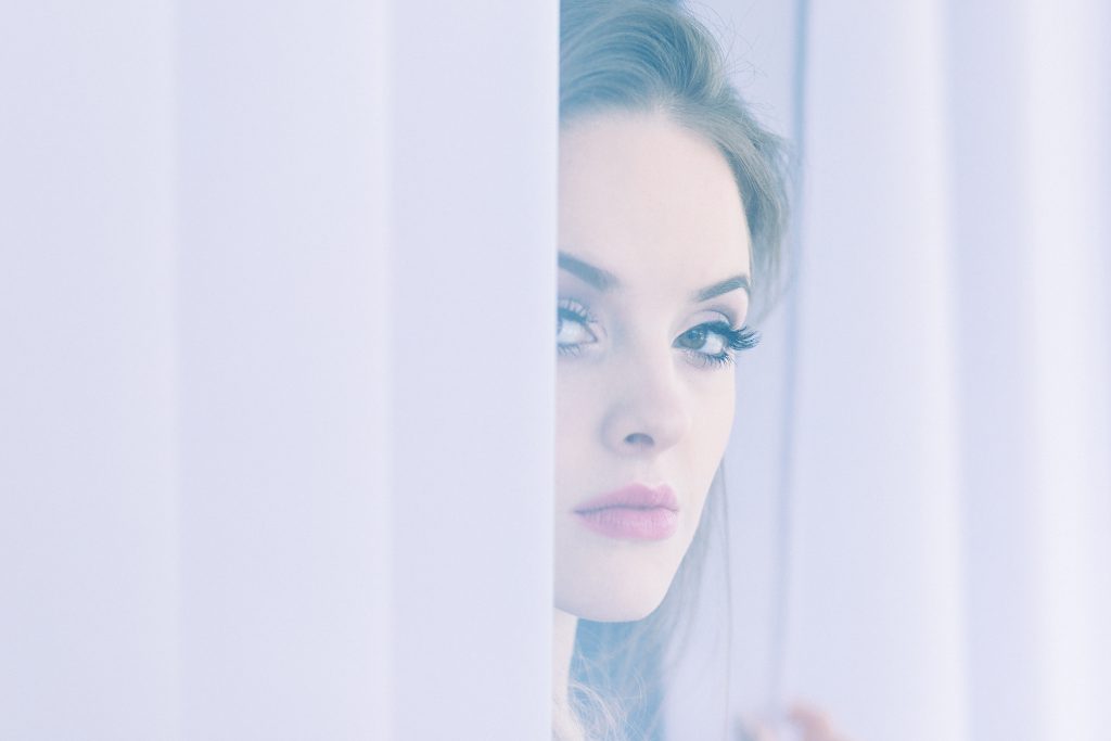 A woman peering through curtains - free stock photo