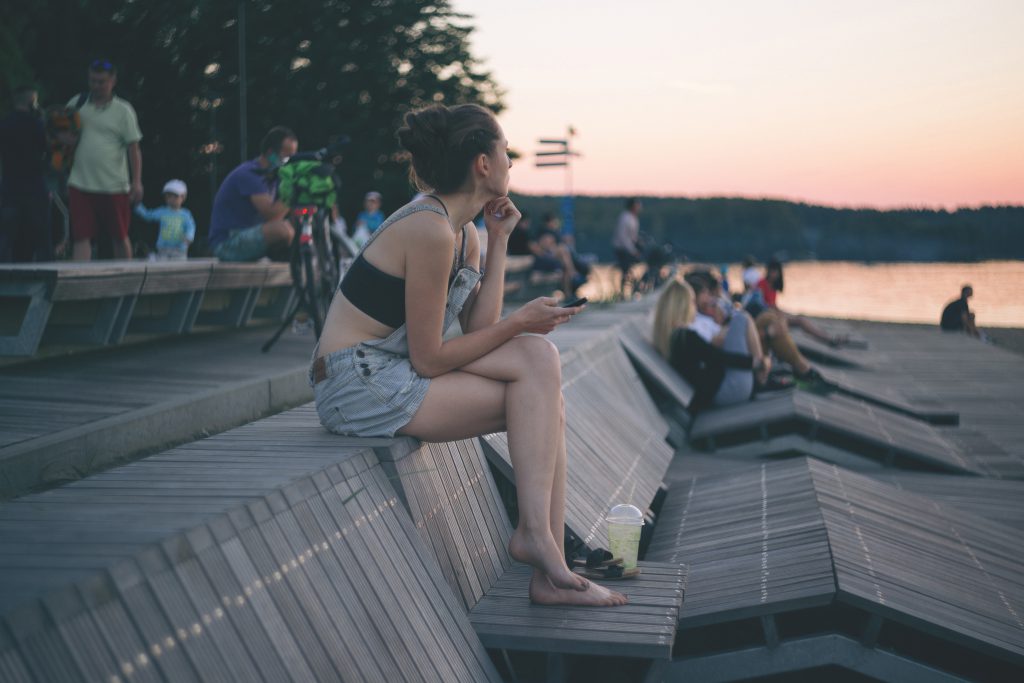 A girl with the phone sitting at the lake - free stock photo