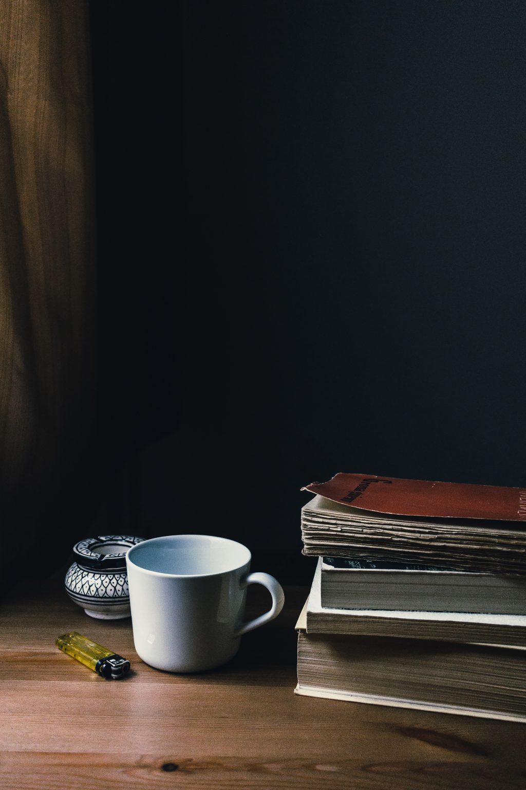 Tea mug, a lighter and a pile of books - free stock photo