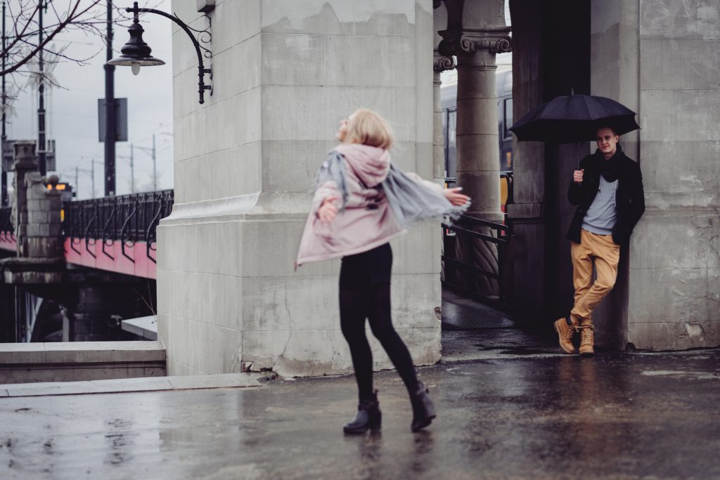 Young man watching his girlfriend dance in the rain - free stock photo