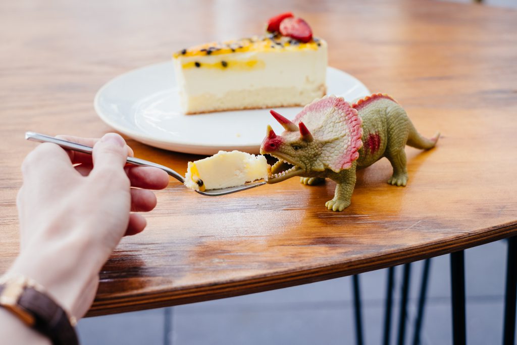 Pretending to feed cake to a rubber toy dinosaur - free stock photo