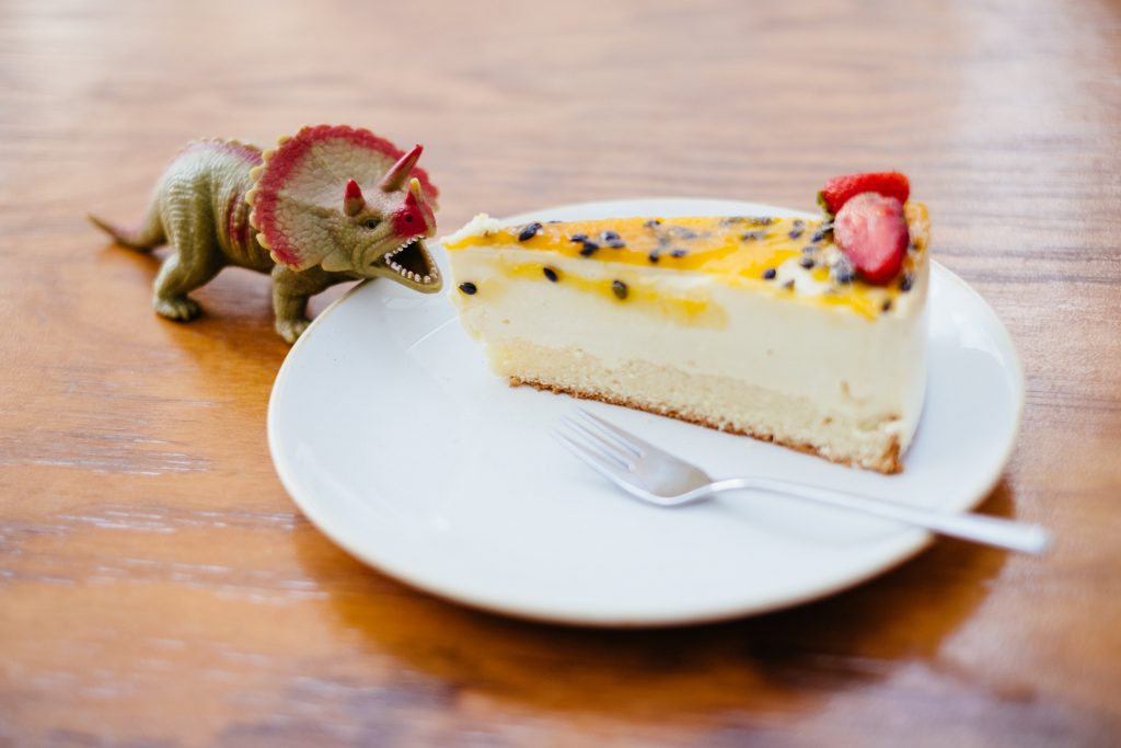 Rubber toy dinosaur about to eat a cake - free stock photo