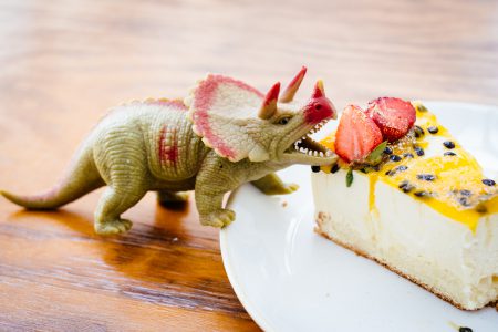 Rubber toy dinosaur about to eat a strawberry on a cake - free stock photo