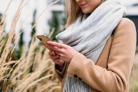 Smiling female holding her phone on an autumn day - free stock photo