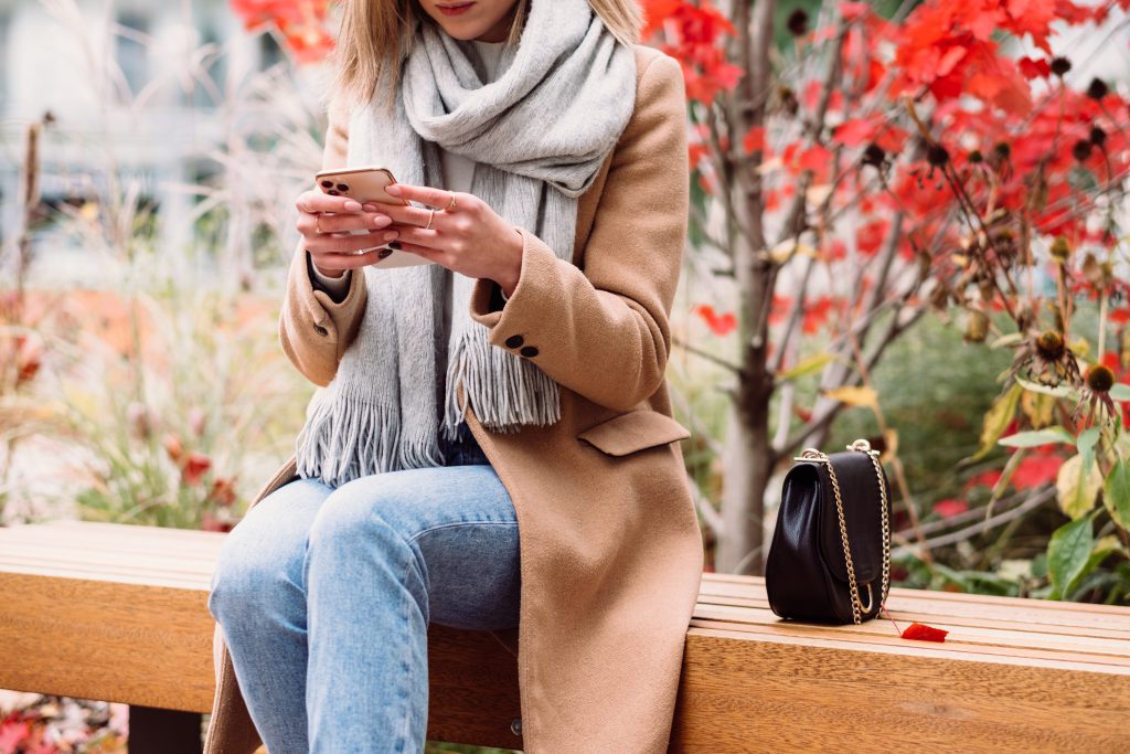 female sitting on a bench and using her phone on an autumn day