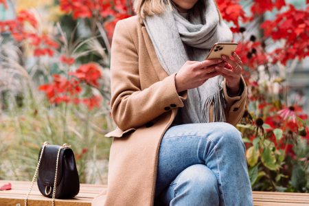 A female sitting on a bench and using her phone on an autumn day 2 - free stock photo