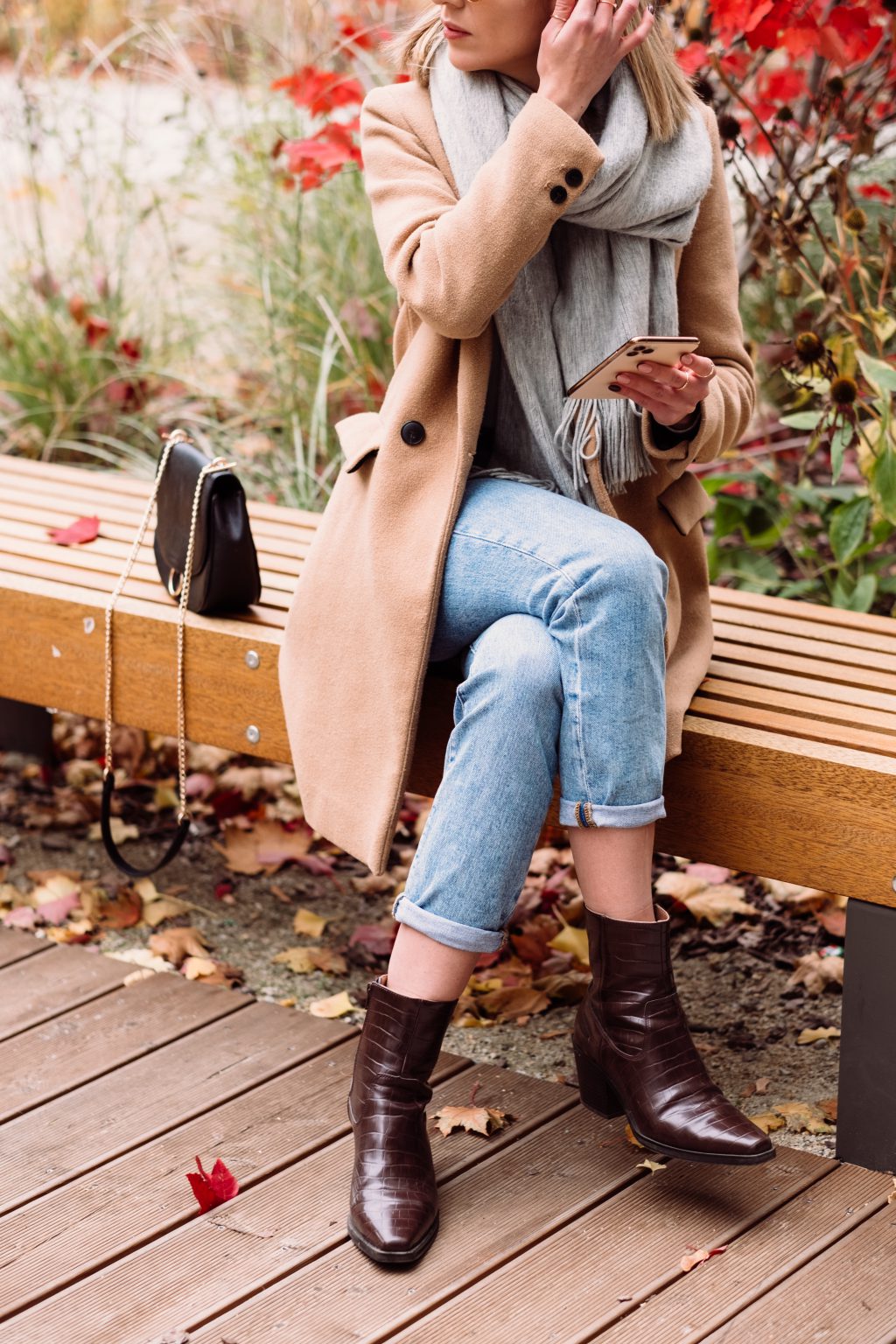 female sitting on a bench and using her phone on an autumn day 3