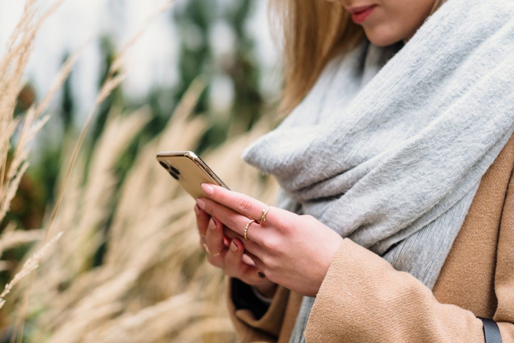 A smiling female holding her phone on an autumn day 2 - free stock photo