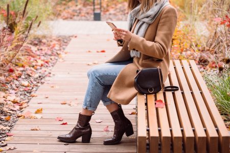 Female sitting on a bench and using her phone on an autumn day 5 - free stock photo