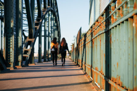 Two females walking across a rusty industrial overpass - free stock photo