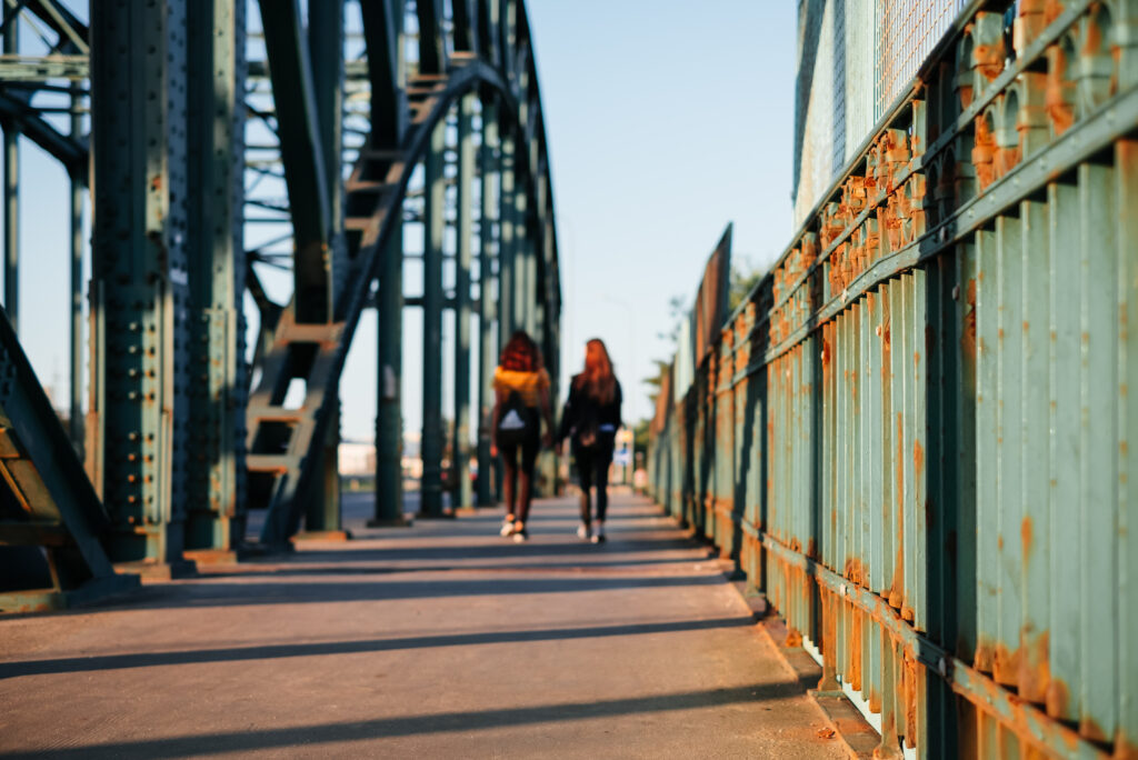 Two females walking across a rusty industrial overpass 2 - free stock photo
